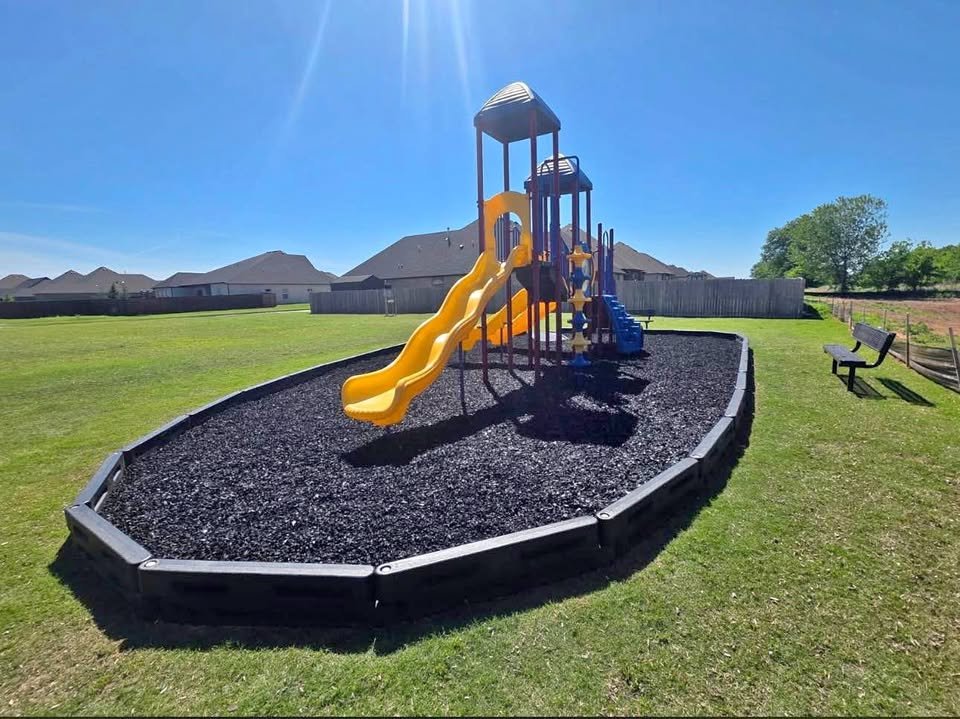 Neighborhood playground surfaced with unpainted black rubber mulch inside a bordered bed